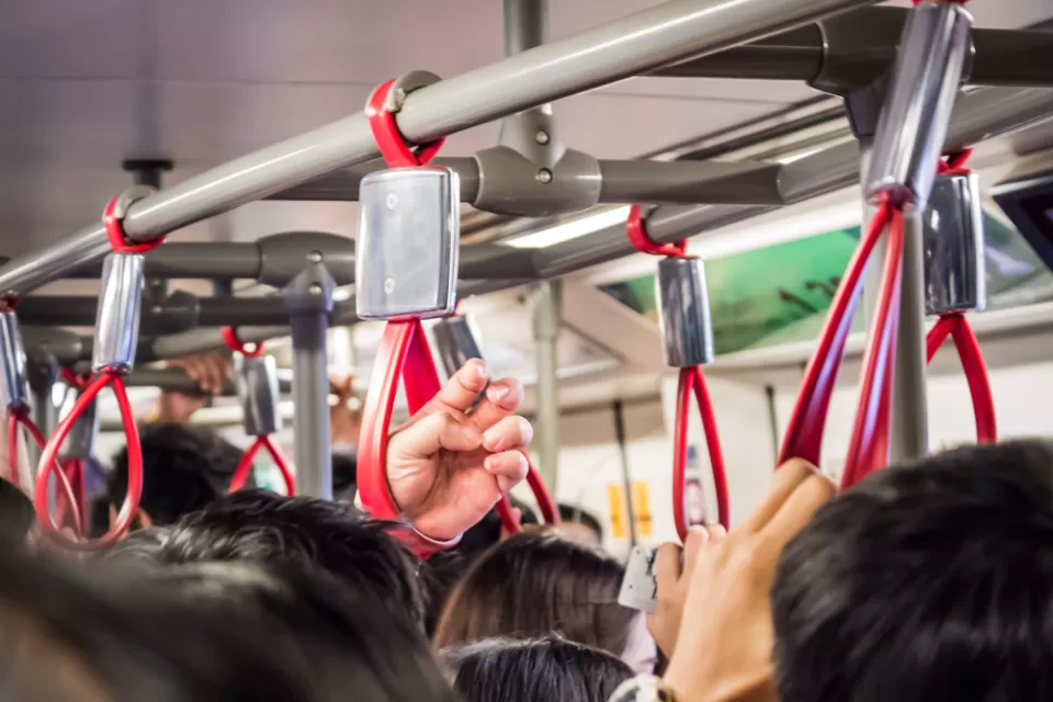 Close-up of bus passengers hanging on to red straps on crowded bus